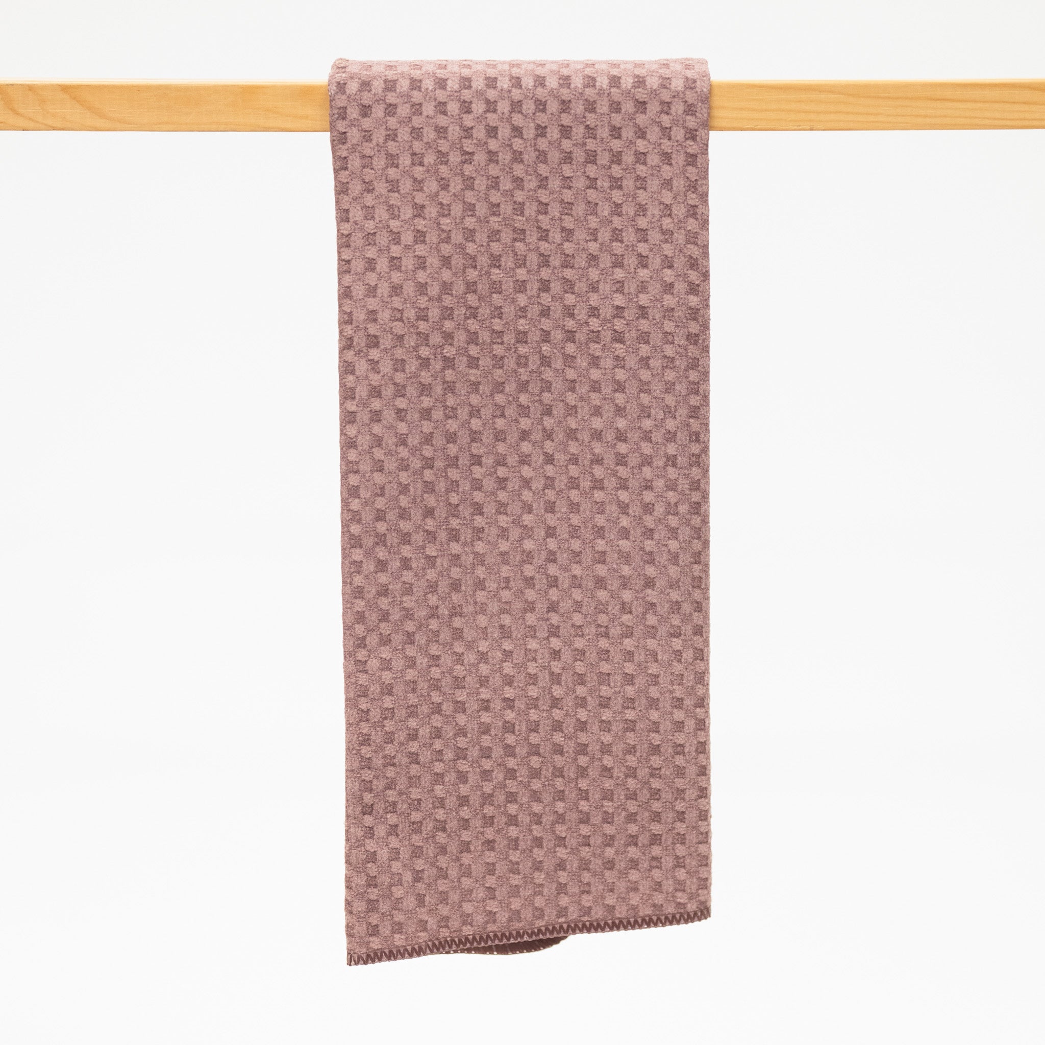 Taupe textured kitchen towel hanging on a wooden rod against a white background