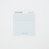 A square white notepad with a light blue grid pattern, labeled 'CLOTH & PAPER' and 'GRAPH | ADPEN', centered on a plain white background.