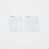 Two small white paper pads labeled CLOTH & PAPER, one with horizontal lines and one with a light blue grid, shown on a plain white background.