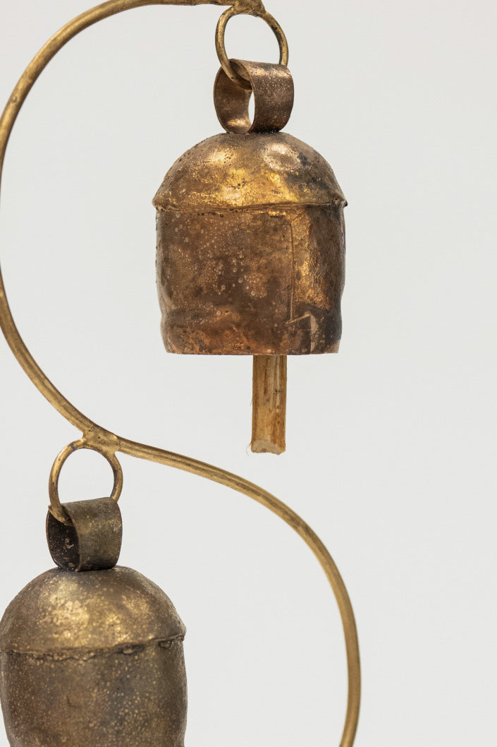 Two brass bells hanging from a curved brass rod on a white background
