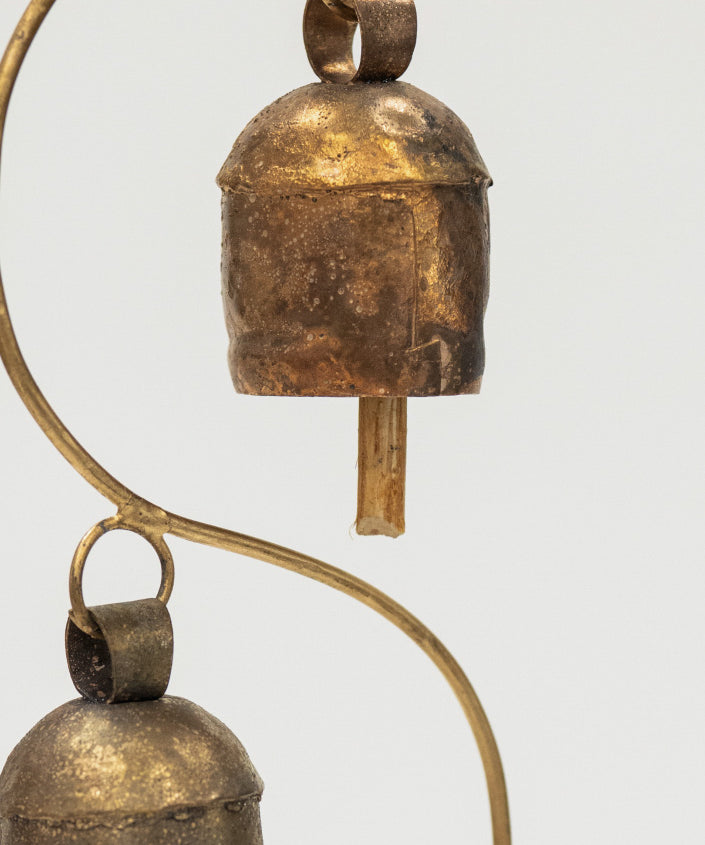 Two brass bells hanging from a curved brass rod on a white background