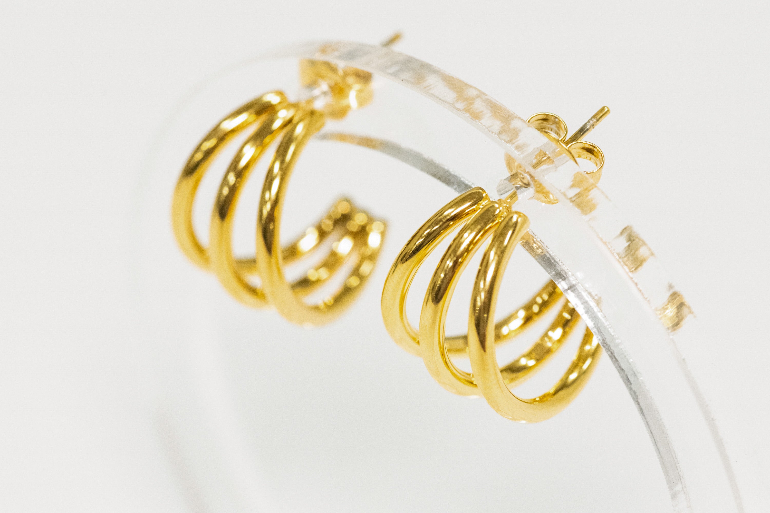 Gold hoop earrings on a clear stand against a white background
