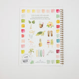 A spiral-bound watercolor painting guide book by Amy Lee Studio, featuring tropical illustrations such as a turtle, pineapple, flamingo, and surfboards on a white cover, photographed on a light gray background.