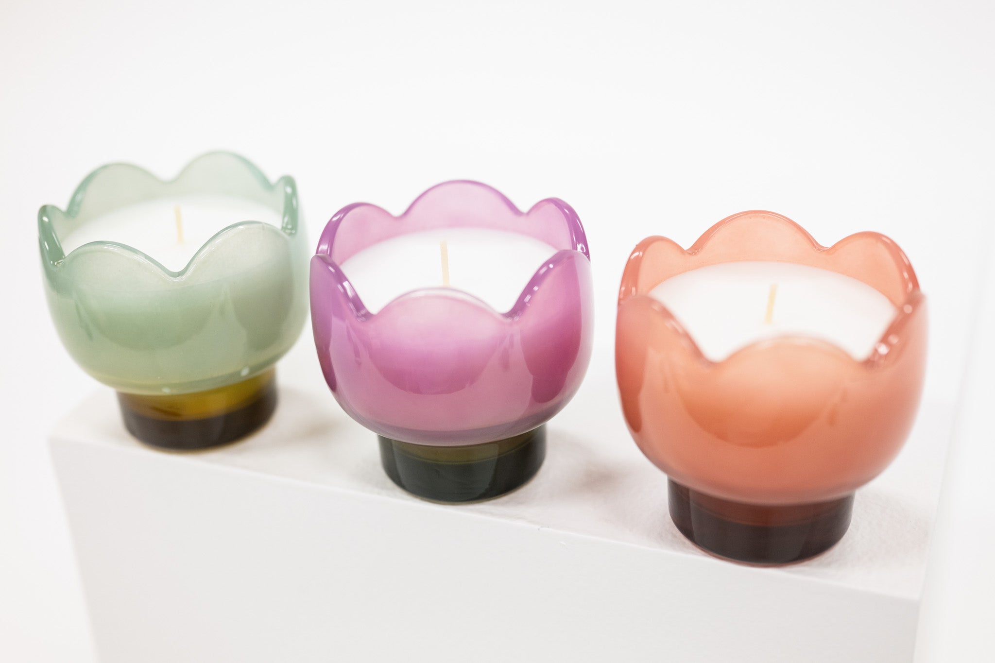 Three colorful glass candle holders with candles inside on a white background