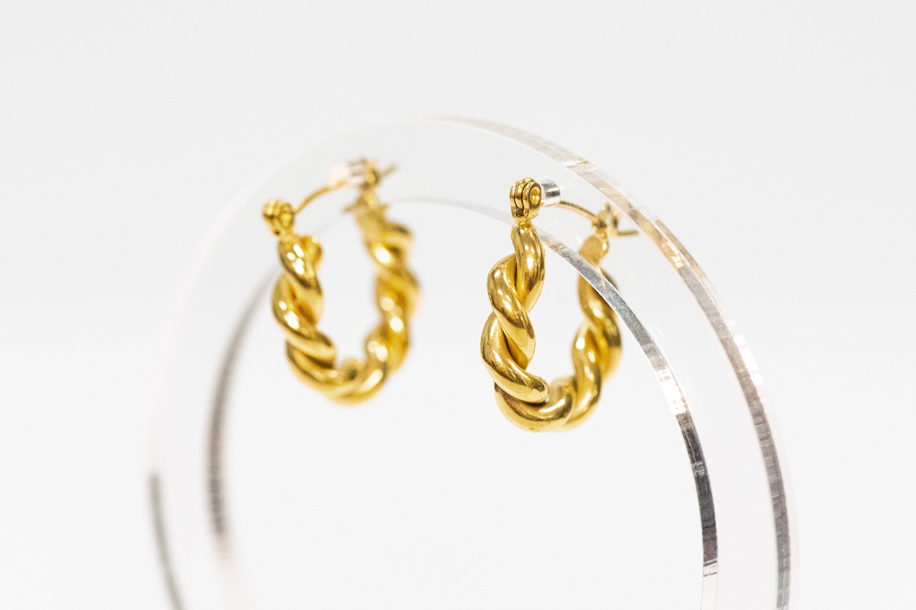 Gold hoop earrings on a clear stand against a white background