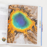 Open book showing a colorful natural landscape illustration on a white background