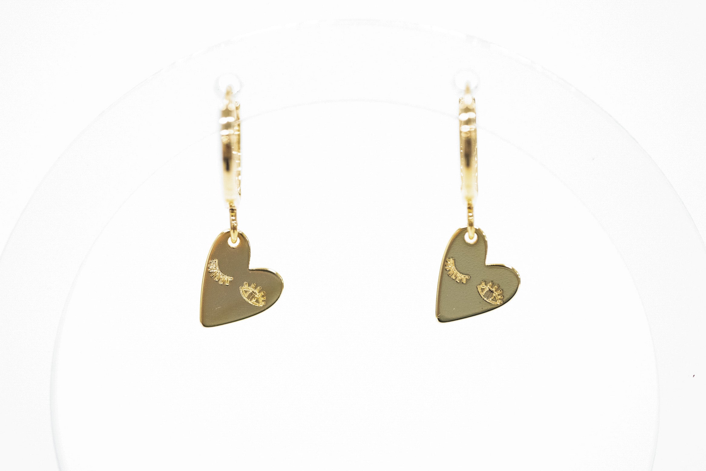 A pair of gold leverback earrings with small heart-shaped charms engraved with crescent moons and stars, displayed on a clean white background.