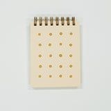 Small light yellow notepad with gold floral patterns on a light gray background
