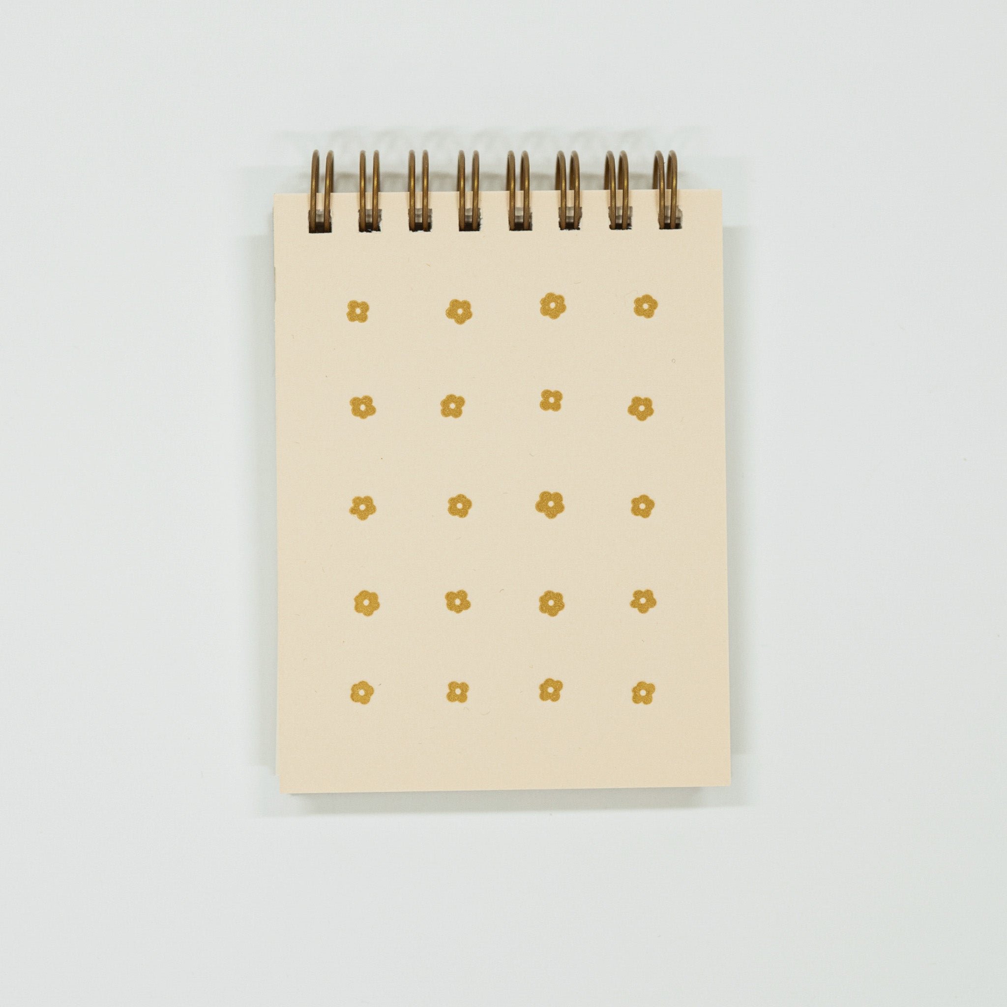 Small light yellow notepad with gold floral patterns on a light gray background